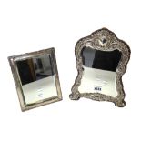 A silver mounted shaped rectangular strut backed mirror, with a floral and scroll embossed border,