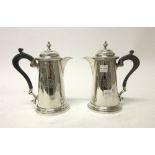 Two silver hot water jugs, each of tapered cylindrical form, with a scrolling composition handle,