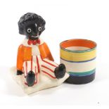 A Clarice Cliff Golliwogg pencil pot the seated Golliwogg with orange jacket and red striped