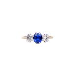 A gold, sapphire and diamond set three stone ring, claw set with an oval cut sapphire at the centre,