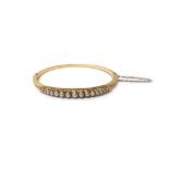 A gold and half pearl set oval hinged bangle, the front mounted with a row of graduated half pearls,