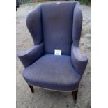 A Georgian winged armchair upholstered in a worn grey upholstery and terminating on square tapering