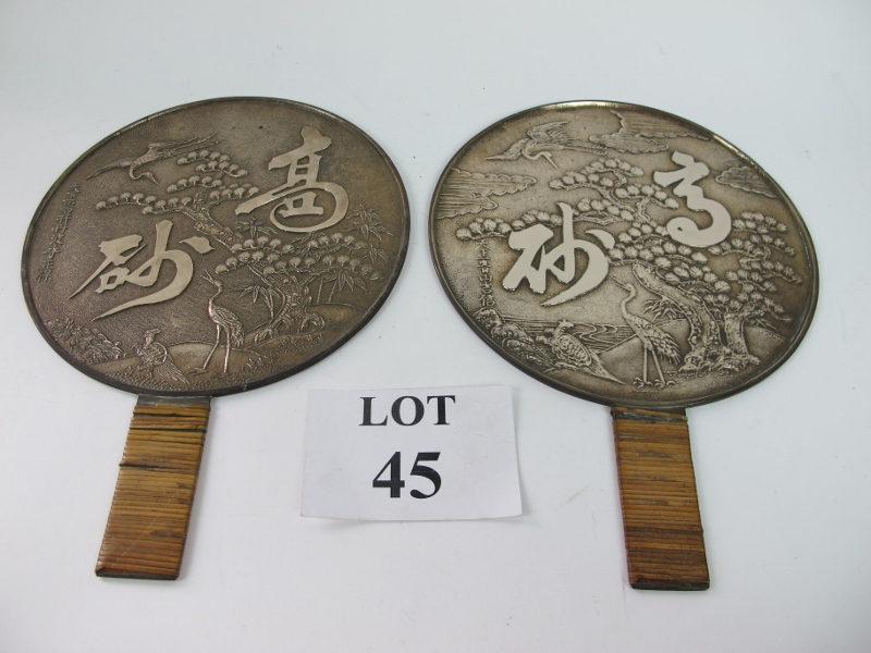 A pair of Chinese white metal polished hand mirrors decorated to reverse with embossed scene