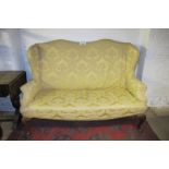 A c1900 high back winged sofa with a loose yellow upholstered cover over carved cabriole legs est: