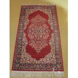 A 20c small Persian design rug on red gr