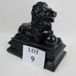 A Regency style ebonised model of a recumbent lion on plinth,