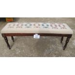 A Victorian long footstool upholstered in cream and floral tapestry material and terminating on