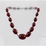 AN EARLY 20TH CENTURY GRADUATED AMBER BEAD NECKLACE of red colour, having brass screw fastener,