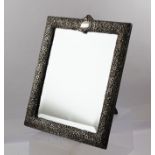HENRY MATTHEWS AN EDWARDIAN SILVER MOUNTED EASEL MIRROR, repousse floral decoration with blind