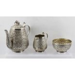 A COLONIAL "INDIAN SILVER" THREE PIECE TEASET IN THE KUTCH MANNER, repousse decoration of flowers