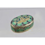 A CONTINENTAL SILVER GILT PILL BOX inset blue and green enamel, the repousse cover with a panel of