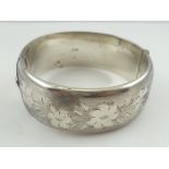 A BROAD SILVER BANGLE with engraved Victorian design decoration