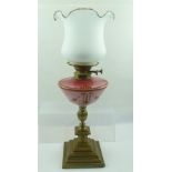 A LATE VICTORIAN OIL LAMP with decorative pink glass reservoir on a brass pedestal and stepped base,