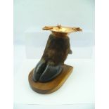 A NOVELTY ASHTRAY FORMED FROM A COW'S HOOF, fitted a polished copper top and raised on wooden shield