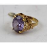 A LADY'S DRESS RING, with an oval cut amethyst type stone, set in a decorative mount with leaf