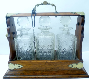 A THREE BOTTLE TANTALUS in oak frame with decorative brass detail, containing three square