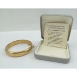 A 9CT GOLD BANGLE of hinged form, the clasp with safety chain, one half is plain, the other with