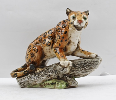 A LATE 20TH CENTURY CONTINENTAL PORCELAIN MODEL OF A LEOPARD, crouched upon a log, printed factory