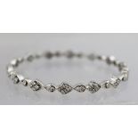 A WHITE GOLD MULTI DIAMOND SET BANGLE in a pierced alternating arrangement of single and cluster