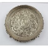 AN INDIAN WHITE METAL DISH, embossed decoration of acanthus leaves about a central peacock