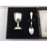 A 1930's SILVER EGG CUP, decorated with female golfer panel, London 1938, with a SILVER SPOON, cased