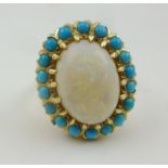 AN OPAL SET LADY'S RING, the central oval stone surrounded by eighteen turquoise stones, set in