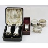 THREE SILVER NAPKIN RINGS, one in a silk and velvet lined case, a PAIR OF SILVER CONDIMENTS,