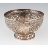 A Victorian silver rose bowl, featuring repousse floral and scrolling foliage design, raised on a