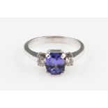 A tanzanite and diamond three stone ring, set with a central cushion cut tanzanite, measuring