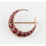 An Edwardian 9ct yellow gold garnet and diamond crescent pin brooch, set with thirteen graduated