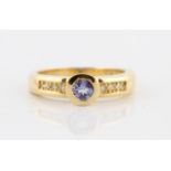 A tanzanite and diamond ring, bezel set with a central round cut tanzanite, measuring approx. 4mm,