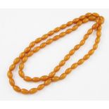 A string of approx. 63 barrel shaped butterscotch coloured plastic beads, length approx. 124cm.
