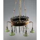 A large brass ceiling light fitting with six green glass shades with fleur de lid decoration to