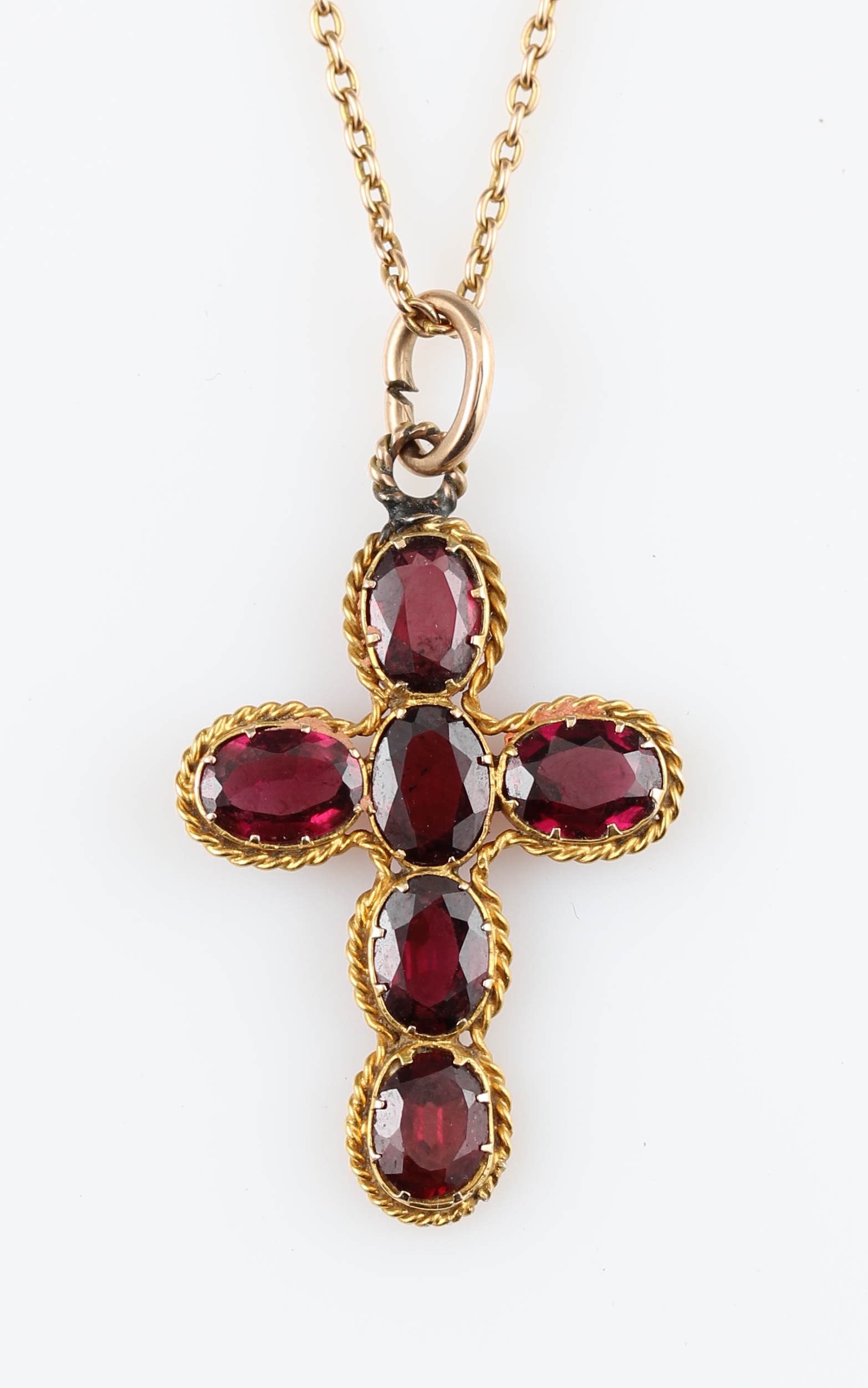 A garnet cross pendant, set with six oval cut garnets, in an unmarked yellow metal mount, on a