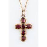 A garnet cross pendant, set with six oval cut garnets, in an unmarked yellow metal mount, on a
