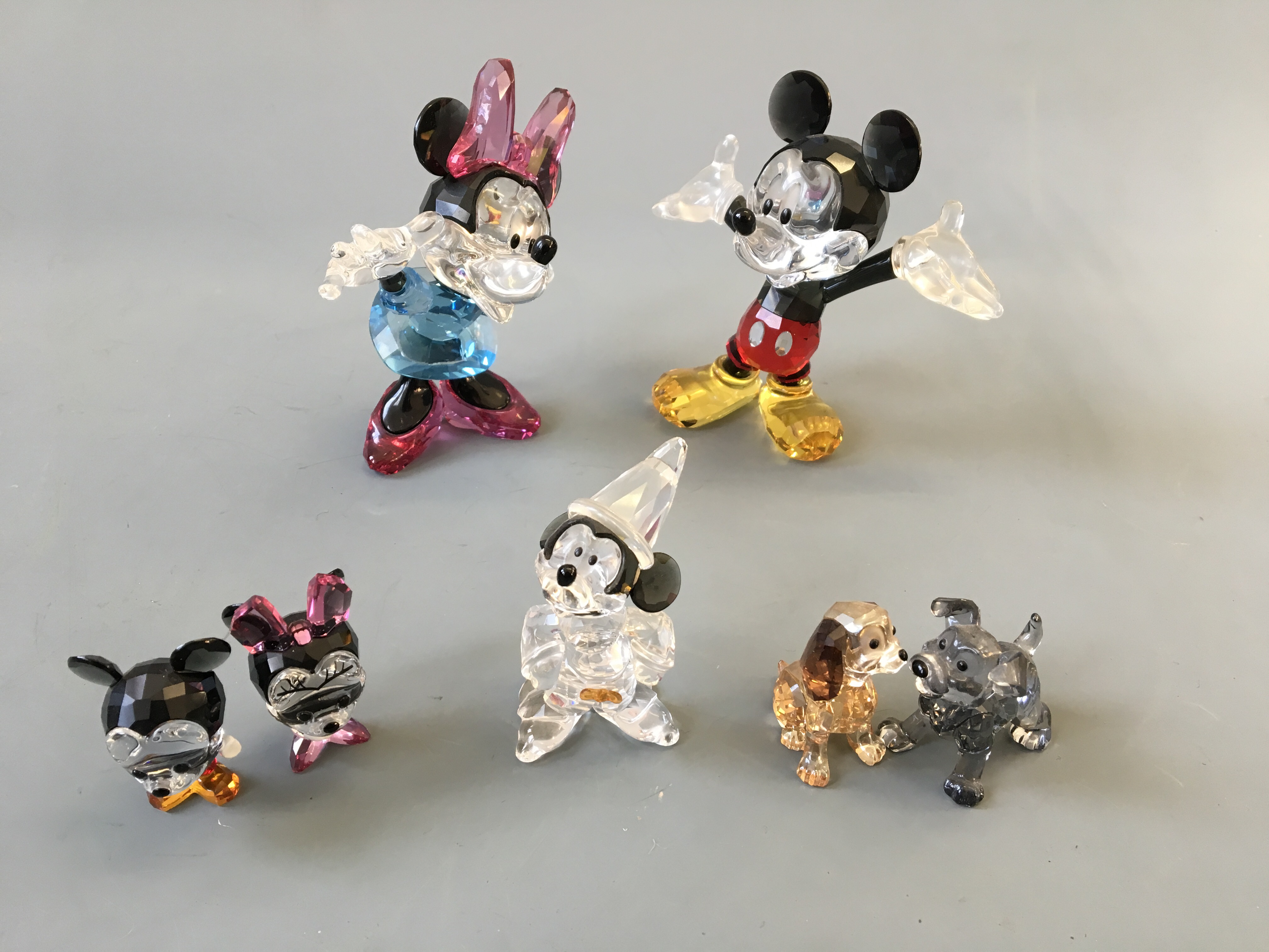 Two sets of Swarovski Mickey Mouse and Minnie Mouse figurines, one set miniature, with The Sorcerers