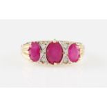 *A 9ct yellow gold three stone ruby ring with diamond accents, set with three graduated oval cut