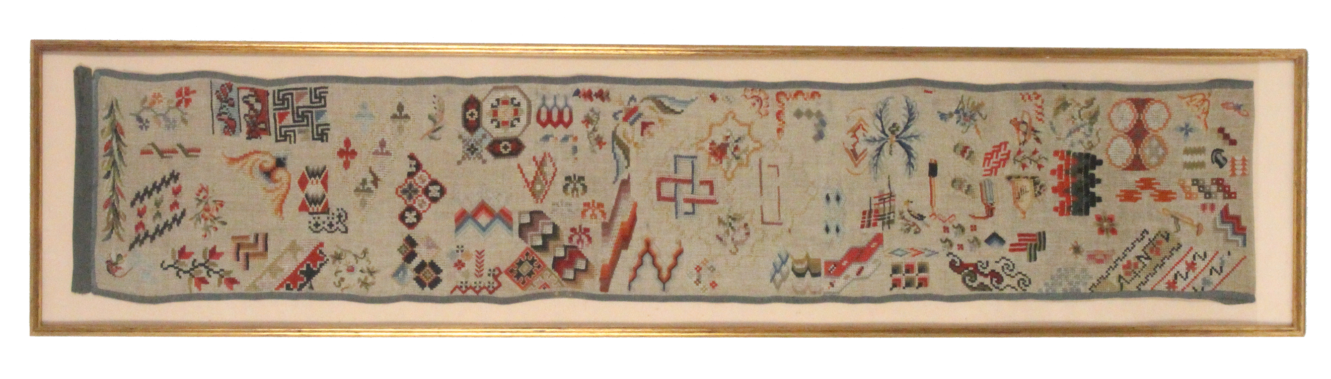 A 19th Century spot strip sampler worked in coloured wools with geometric motifs, leaves, flowers