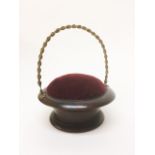 A turned mahogany basket form pincushion with gilt metal 'rope' swing handle 15cm dia.