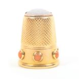An early 20th Century gold thimble with opaque stone inset top, the frieze with six coral coloured