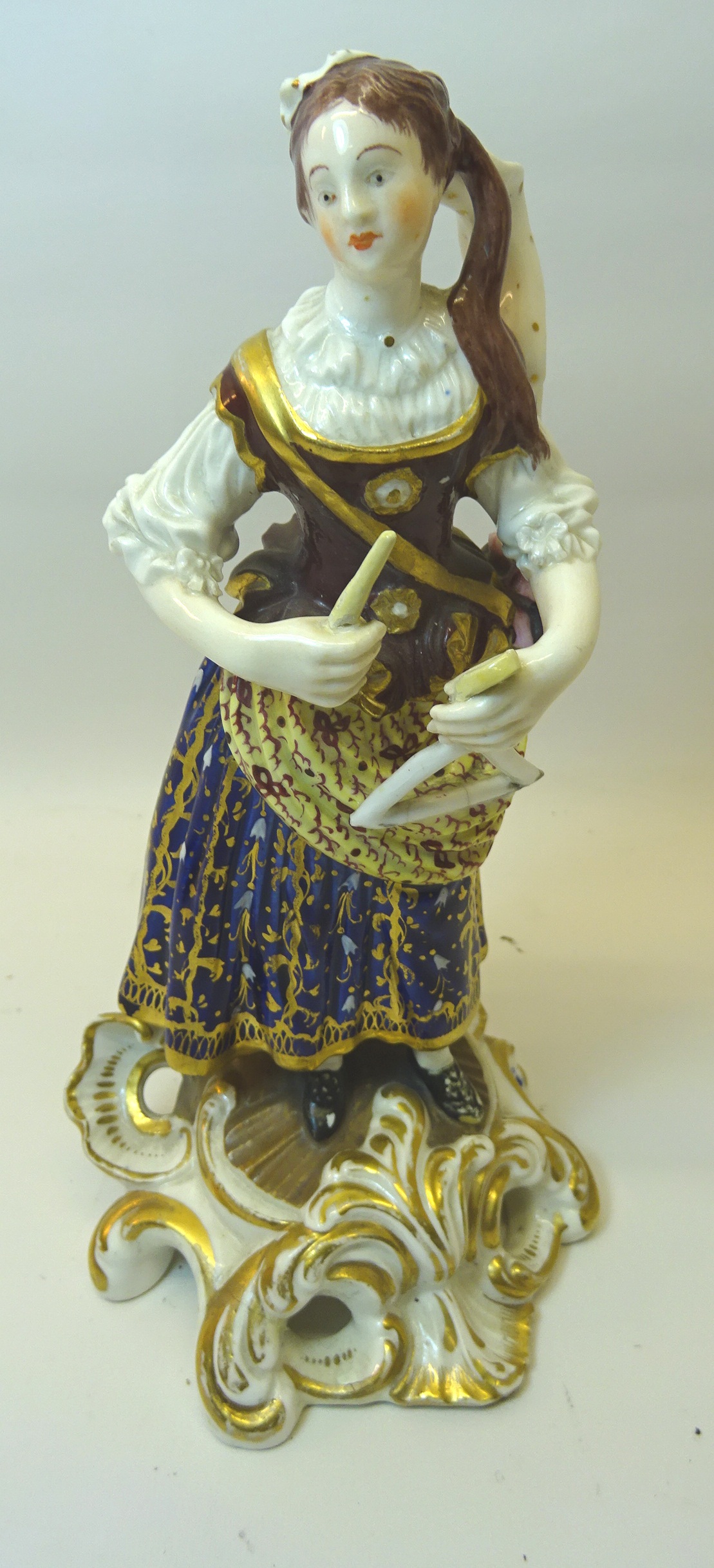 A 19th Century Continental standing female Figure playing a triangle, dress decorated in blue and