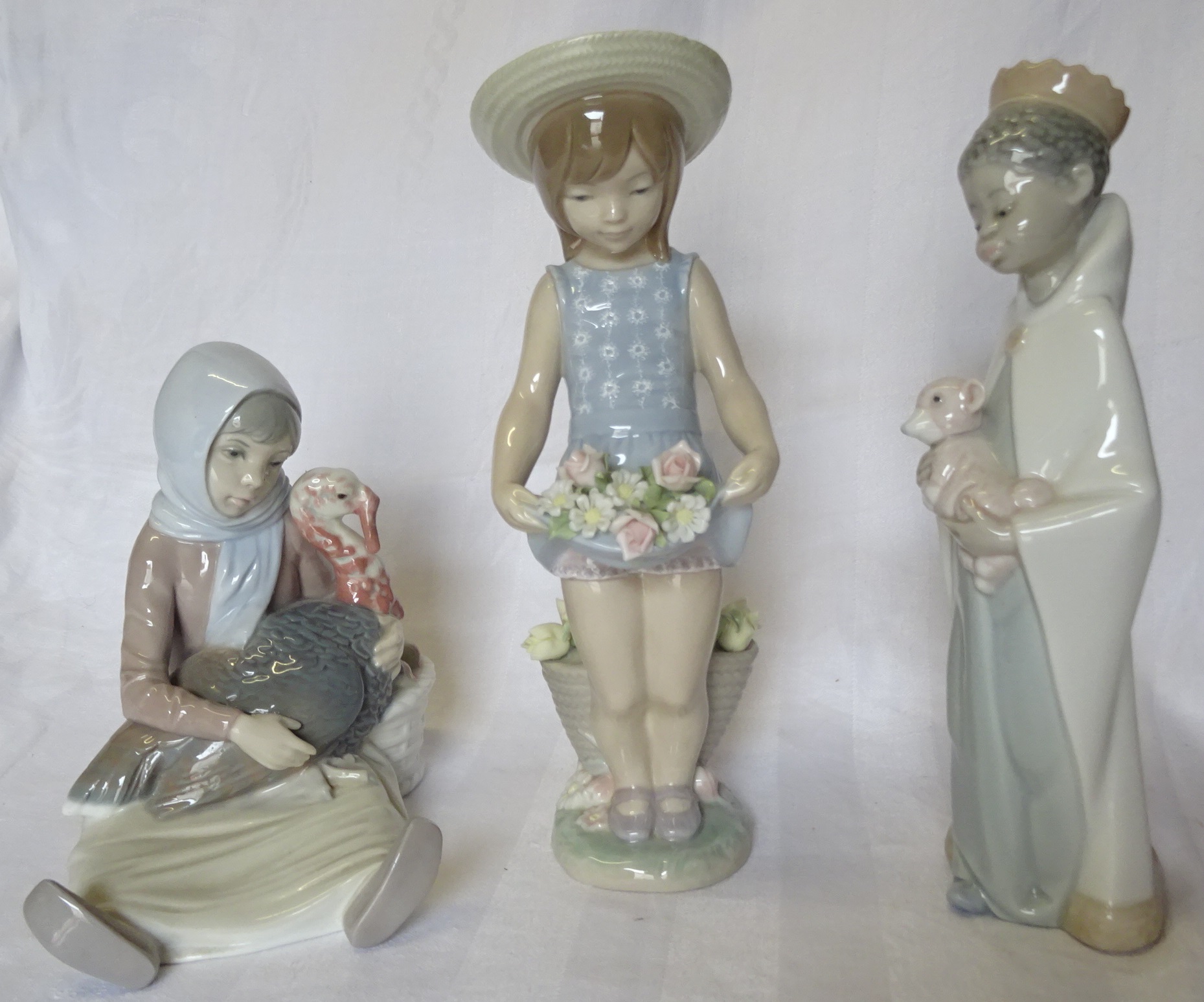 A Lladro Standing Figure of a girl holding flowers, another holding a lamb, and a Seated Figure with