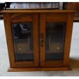 An Edwardian oak Smoker's Cabinet with hinged top and pair of glazed doors, fitted with small