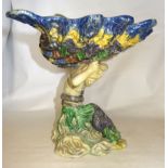 A Majolica Centrepiece in the form of a large shell, surmounted by a lizard, supported by a Merman