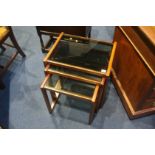 A teak and glass nest of three tables