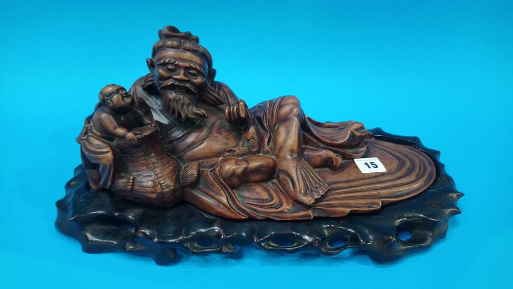 An Oriental hardwood figure of a recumbent fisherman on stand