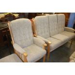 A light wood framed three seater sofa, armchair and footstool