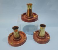 A set of three brass ashtrays on wood bases