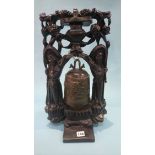 An Oriental hanging bell, set in a carved wood framework and standing on a circular table