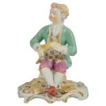 An 18th Century Derby Figure of a Boy: the seated figure wearing a pale green jacket and holding